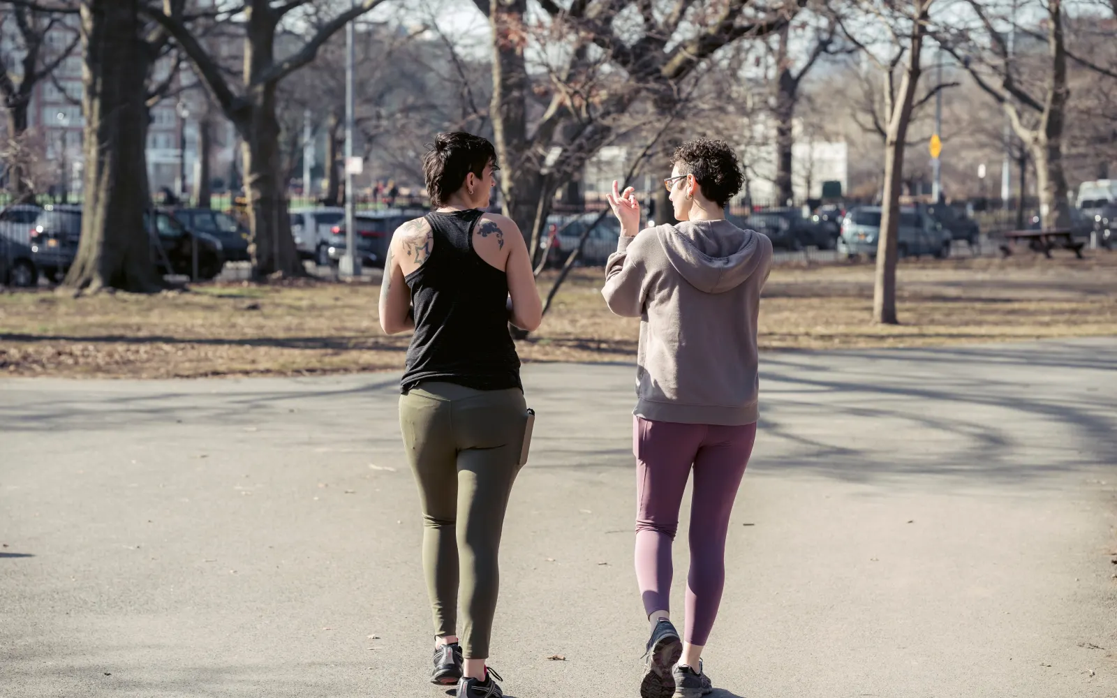 Two women in active clothing walking together through an autumn park