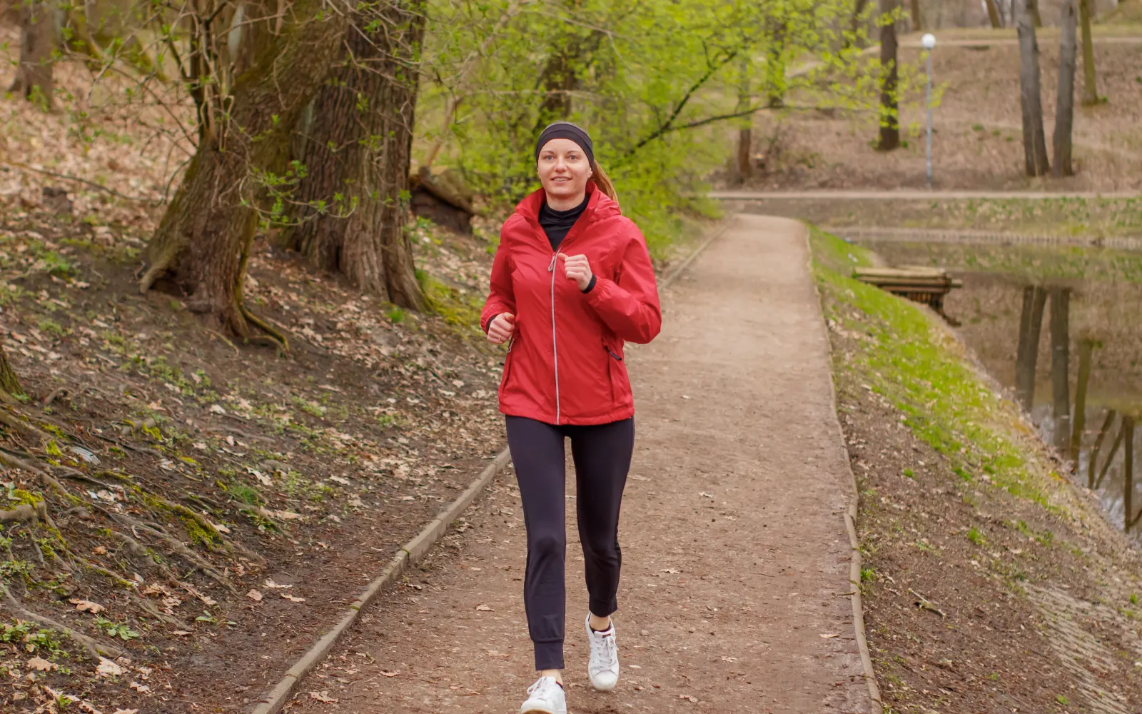 Runner in a red jacket jogging on a park path